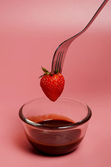 fondue strawberry soaked in hot black chocolate on a fork with pink background with minimalist style .have some spec for write wording