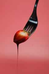 fondue strawberry soaked in hot black chocolate on a fork with pink background with minimalist...