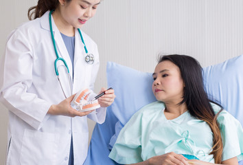 Beautiful woman dentist talking with her female patient explain with tooth model and preparing to treatment at dental center