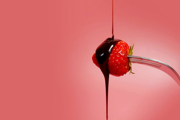 fondue strawberry soaked in hot black chocolate on a fork with pink background with minimalist...