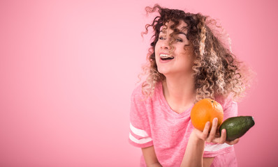 Portrait of a young cheerful girl with curly hair with fruit in her hands