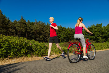 Healthy lifestyle - middle-aged woman riding bike and young man running