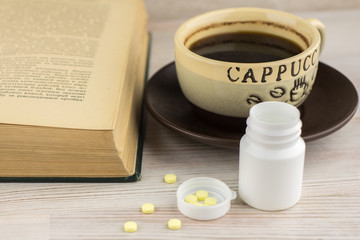 ensuring good employee: a pack of tablets of ephedrine, Cup of strong coffee on a plate, nearby lies an open book, front view, close