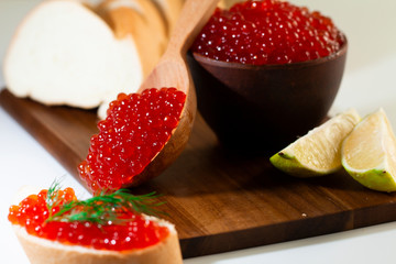 red caviar in a ceramic dish on a wooden platform on a white background
