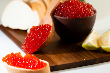 red caviar in a ceramic dish on a wooden platform on a white background