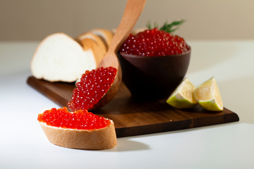 red caviar in a ceramic dish on a wooden platform on a white background