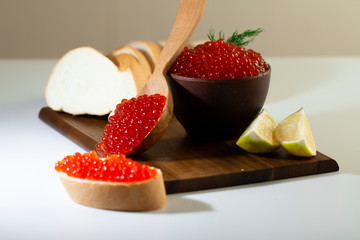 red caviar in a ceramic dish on a wooden platform on a white background