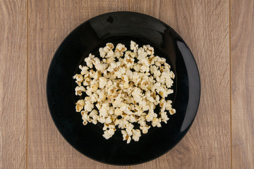Home-cooked in the microwave the popcorn in a black bowl on a wooden table, top view