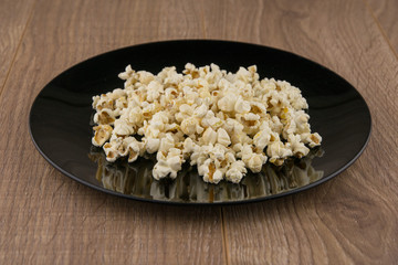 Home-cooked in the microwave the popcorn in a black bowl on a wooden table, front view