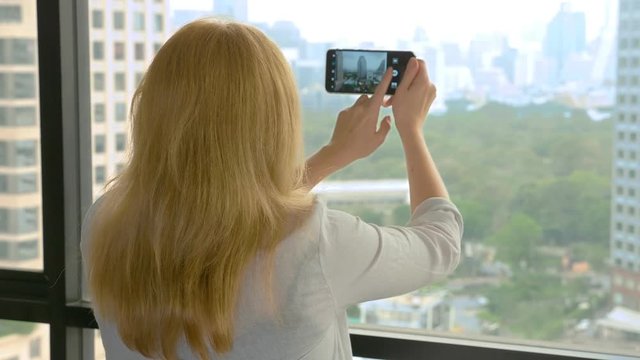 Elegant blonde woman making a photo on the phone. woman photographs the view from the window of the skyscrapers