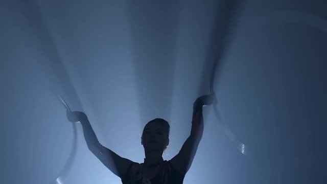 Girl gymnast in the air twists metal hoops with her hands. Slow motion. Smoke background