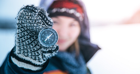 Young woman with gloves is holding up a compass, outside in the winter
