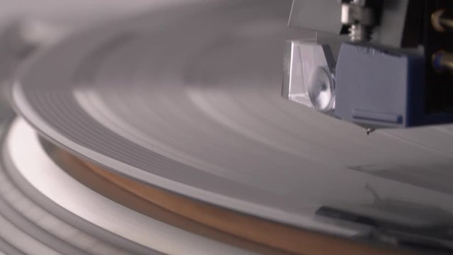 Macro shooting of coil cartridge lifting to vinyl record rotating on the turntable.