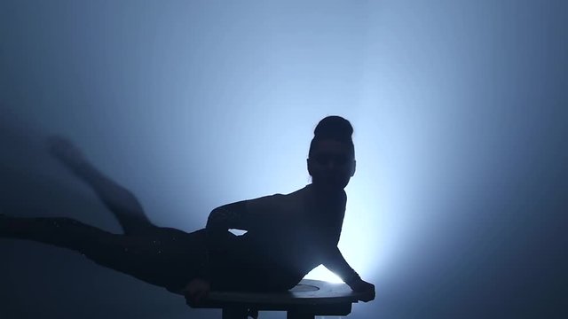 Gymnast on the table sits on the splits. Smoke background. Slow motion. Silhouette