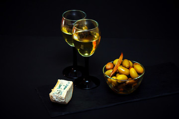 Large pickled green olives in a bowl and white wine in a glass and blue cheese over black background