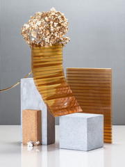 Modern abstract still life using concrete blocks, building construction elements and a golden plant.