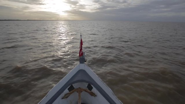 Captain's POV of the bow of a small wooden fishing boat with anchor visible travelling towards the setting sun on the Amazon River in Latin America
