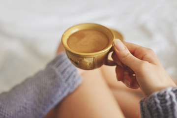 A cup of coffee in their hands in bed on a white blanket, simple, home, space in the frame