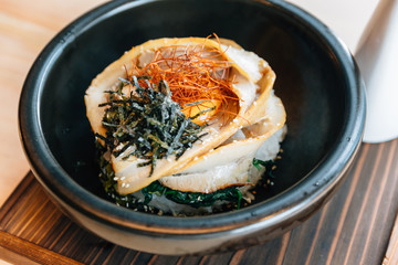 Close up Japanese Chashu Don: Steam Rice topping with Roasted Pork Belly, Yolk, Dried Seaweed and Saffron. Served in black ceramic bowl with Shoyu sauce.