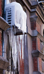 Fototapeta na wymiar Air conditioner covered with ice and icicles. Aged old house wall. Cold cooling concept