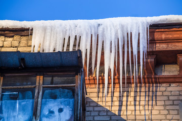 Large icicles hang from a house roof. Dangerous large icicles.