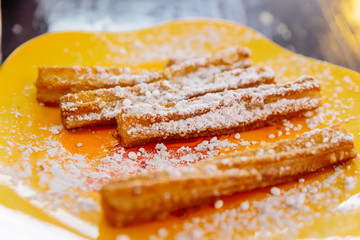 Cloes up Churros topping with icing sugar served with nutella sauce on yellow plate.