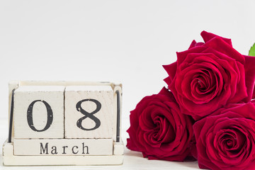 beautiful bouquet of red roses and wooden cube calendar on a wooden background. The concept of congratulations on March 8 or wooman's day.