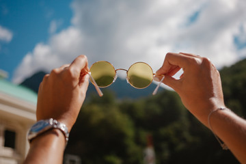 Hands holding yellow round sun glasses over blue sky