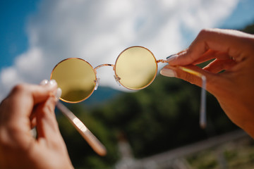 Hands holding yellow round sun glasses over blue sky
