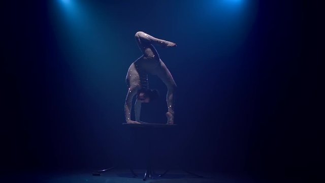 Gymnast on the table shows acrobatic stunts . Smoke blue background. Slow motion