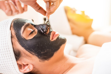 Naklejka premium Close up of Healthy Young Woman getting mud Black and gold facial mask cosmetic procedure in the beauty salon.Skin treatment in spa salon concept