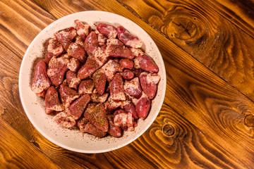 Ceramic plate with raw chicken hearts on wooden table. Top view