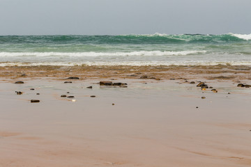 Empty sandy beach. View over the open ocean. Wavy ocean. Cloudy day. Nature scenery.