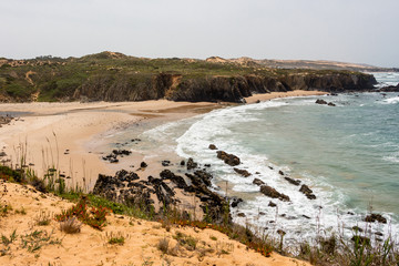 Wild sandy beach with cliffs on Atlantic ocean coast, Atlantic Ocean, Rota Vicentina, Alentejo, Portugal. Small waves hitting the rocks.