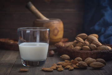 Almond milk in glass with almonds on rustic wooden background in low key.