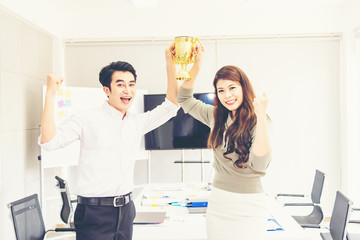 Young happiness asian smart business people holding gold trophy awards together after successful victory business team in modern office. Award trophy winner business teamwork concept.