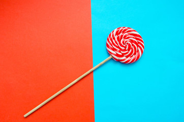 red and white striped round lollipop is lying on a blue-red background