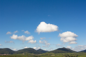 Obraz na płótnie Canvas Idyllische Hügellandschaft unter blauem Himmel mit weißen Wolken