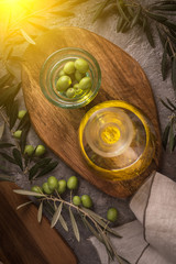 Extra virgin olive oil in glass bottle with branch of olives on rustic background. low key with sun glare from left side.