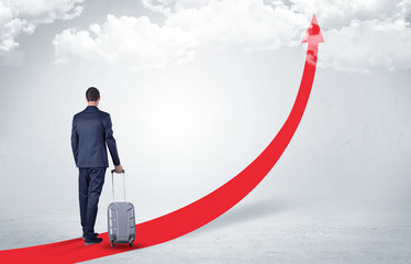 Young businessman with back leaving on the red arrow carpet to the skies with luggage on his hand
