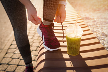 Green detox smoothie cup and woman lacing shoes before workout.