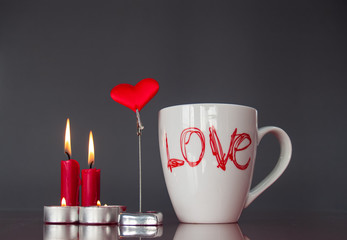 Concept of love Still life with red lit candles, a red heart and a breakfast cup with the word love