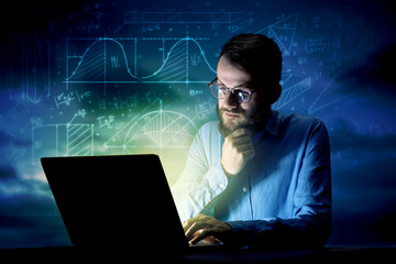 Young handsome businessman working late at night in the office with blue mathematic charts in the background