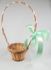 Beautiful wicker basket of light brown color with a tiffany-colored bow tied on a white background