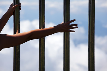 hand in jail with cloudscape background.