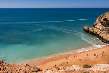 Aerial view over the Benagil beach, cliffs and turquoise ocean. People on the beach enjoying on a beautiful, sunny day.