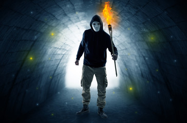 Ugly man with burning flambeau walking in a dark tunnel