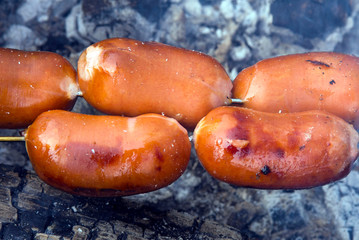 Beautiful, juicy, tasty and fragrant sausages on the grill roasting over coals at a picnic in the winter forest. Around soars smoke and aroma. Meeting with friends.