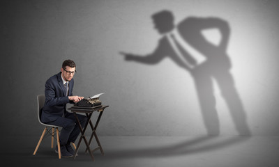 Little man working and a big shadow arguing with him
