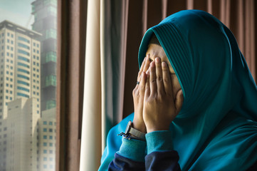 young sad and depressed Muslim woman in Islam traditional Hijab head scarf at home window feeling...